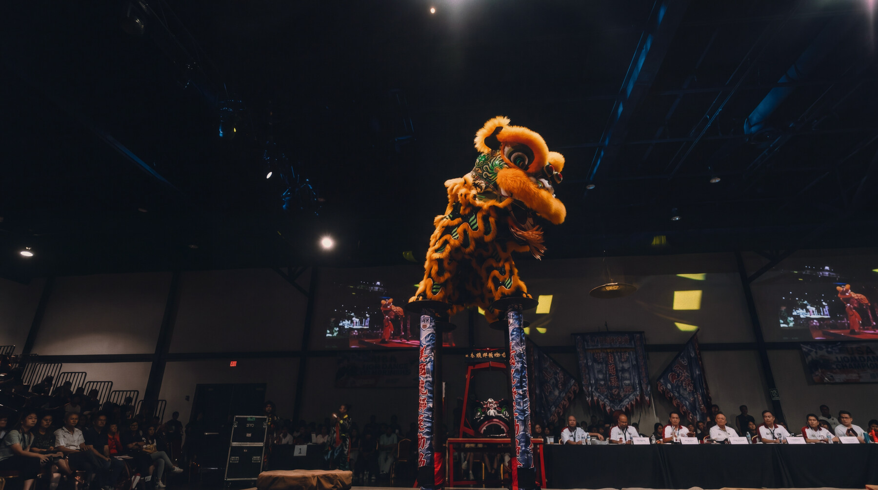 An orange Mak Fai lion mid-leap atop the jong poles at a competition