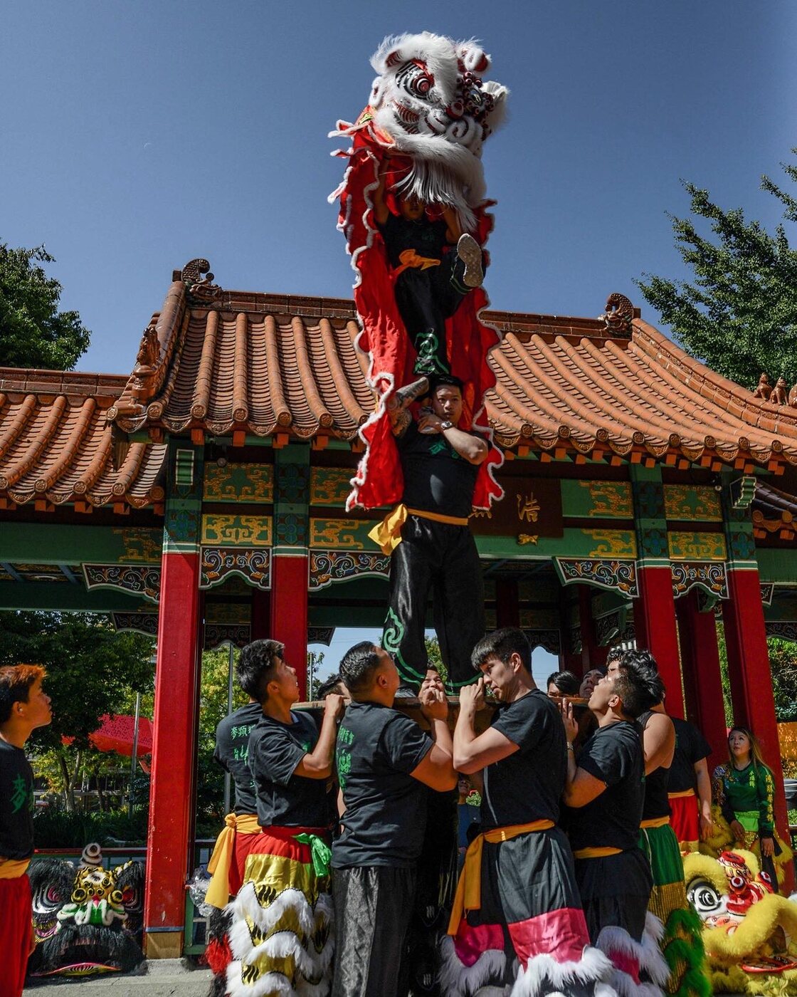 A Mak Fai lion dancer lifted high above a traditional Chinatown gate during a performance